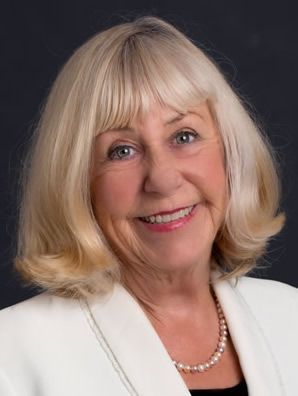A woman wearing a white jacket and a pearl necklace is smiling for the camera. Florence Barrett-Hill