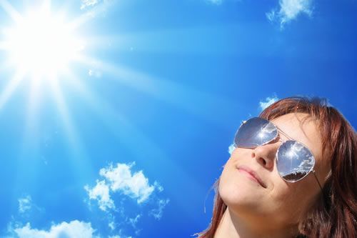 A woman wearing sunglasses is looking up at the sun.