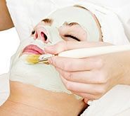 A woman is getting a clay mask on her face.