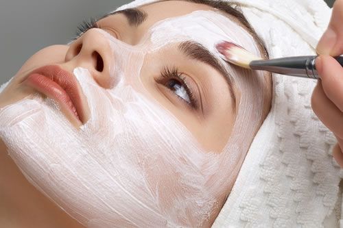 A woman is getting a white mask on her face.