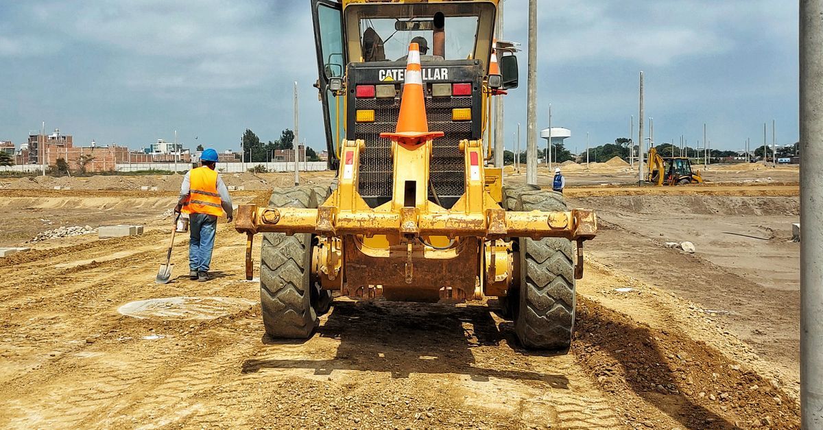 Construction worker beside yellow bulldozer on muddy roadwork site