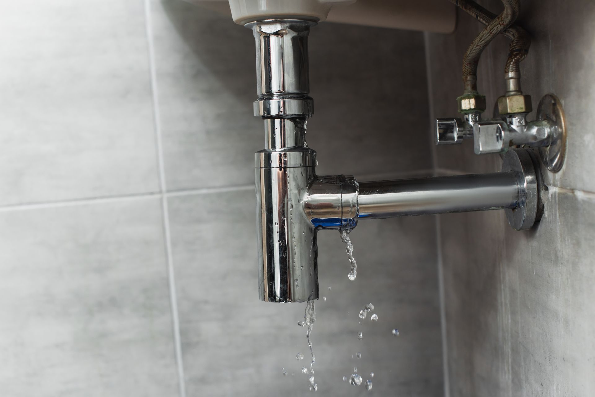 Water is leaking from a sink pipe in a bathroom.