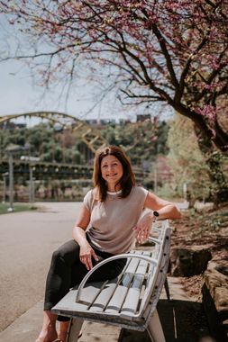 Woman smiling on a bench under pink blossoms in a park