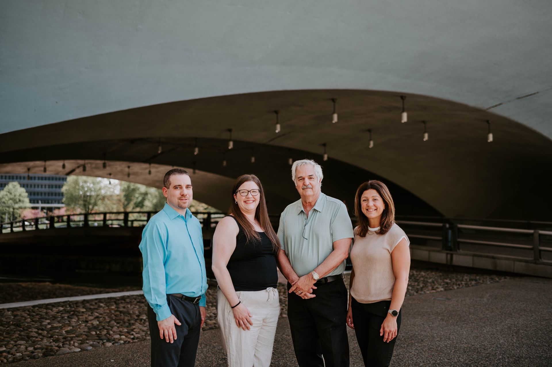 Four people standing under a large curved bridge, posing together outdoors.
