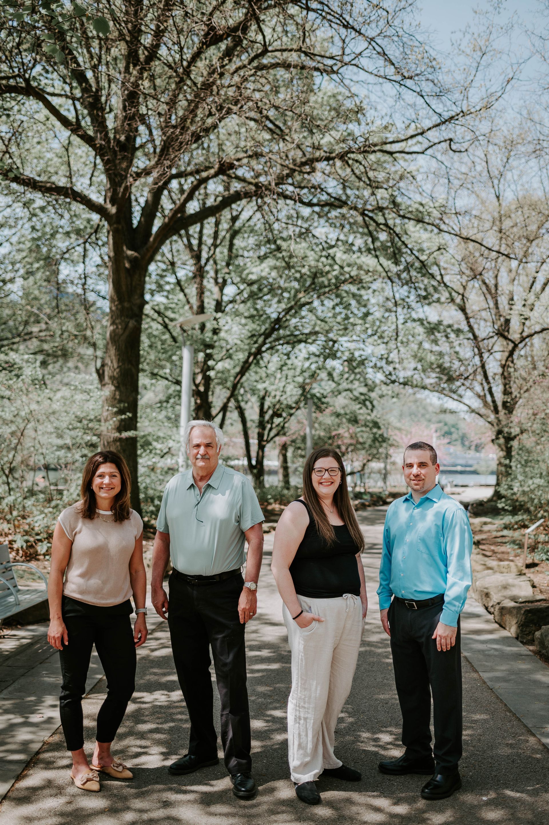Four people standing on a path under trees outdoors, posing for a group photo.