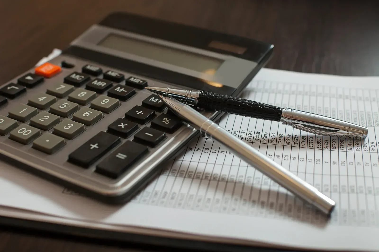 Calculator and pens on a notebook with spreadsheets, in an office setting