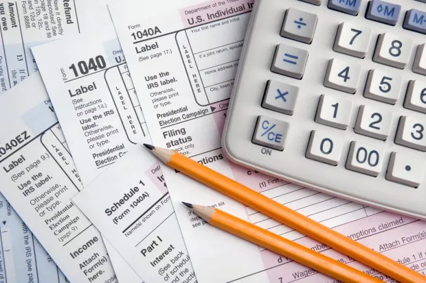Tax forms, pencils, and a calculator on a desk for calculating taxes