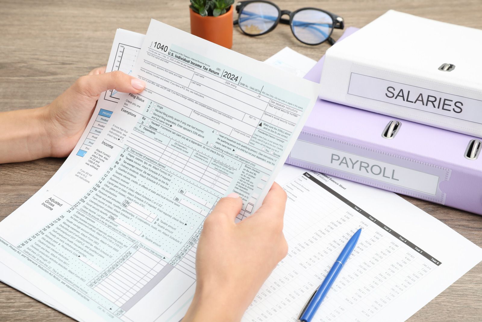 Hands reviewing a tax form at a desk with payroll and salaries folders nearby.