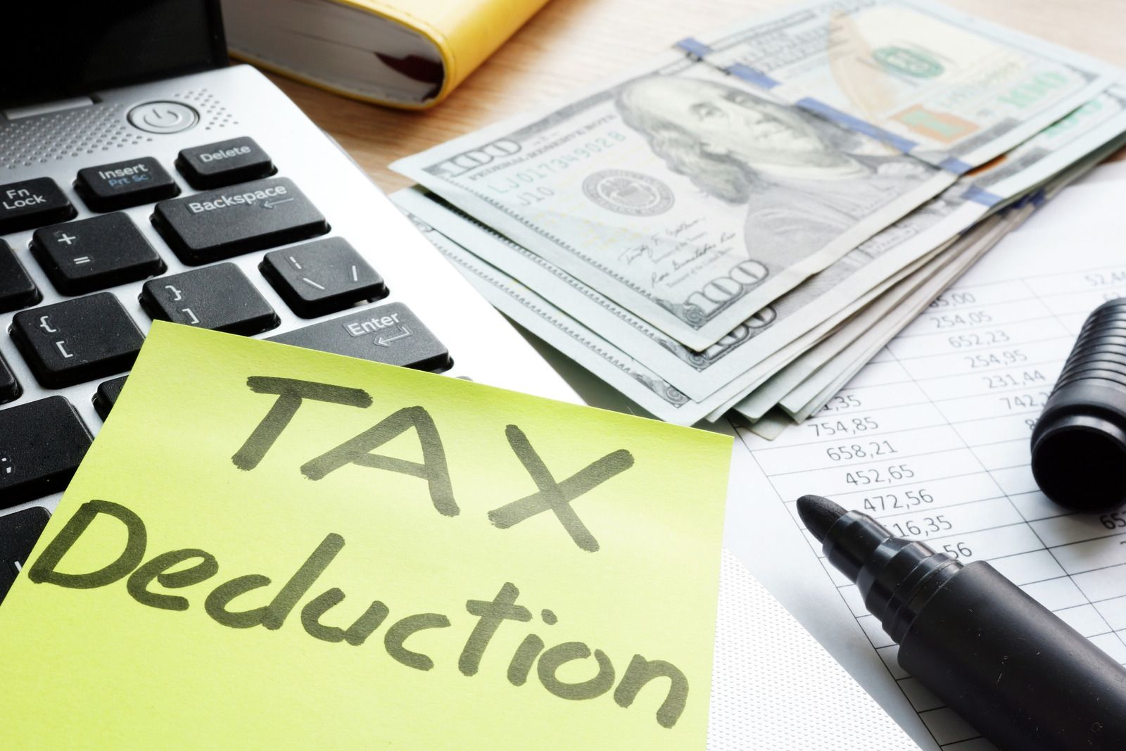 Calculator and cash beside a yellow note reading “Tax Deduction” on a desk