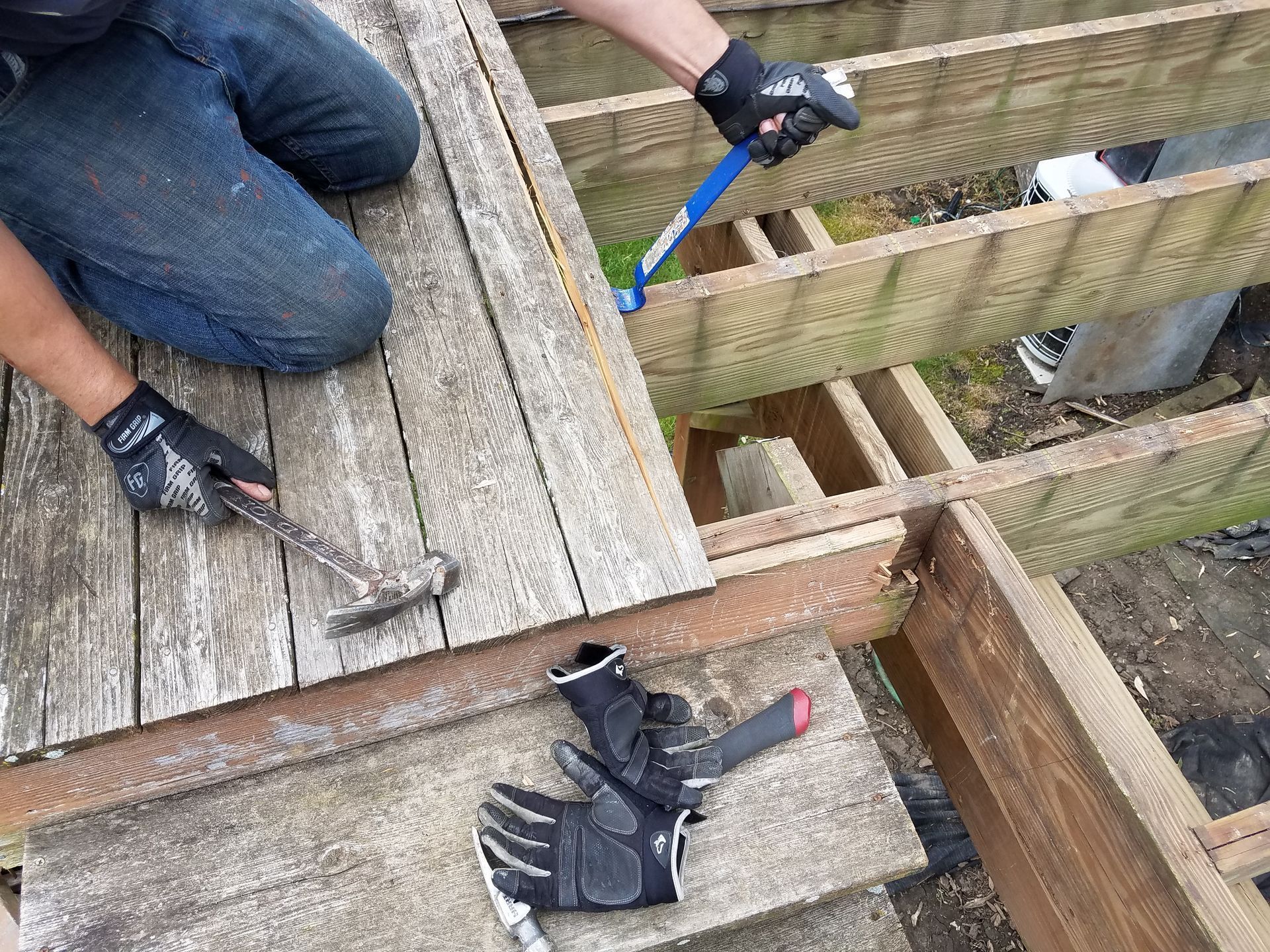 Person removing weathered deck boards with tools.