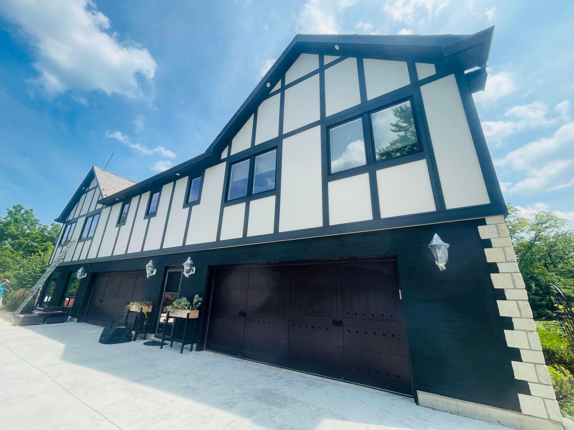 Two-story Tudor house with dark trim and garage doors. Black and white exterior, blue sky.