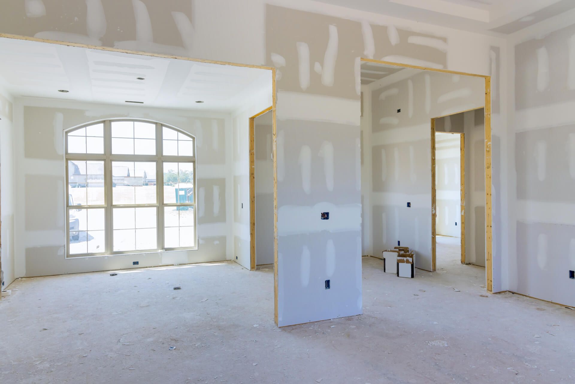 Interior view of a room under construction with exposed drywall, a window, and doorways.