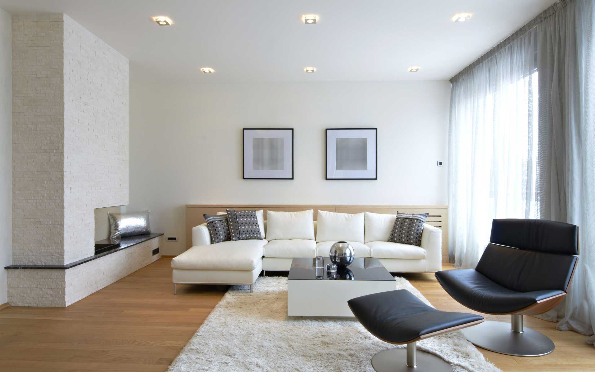Modern living room with white sofa, black chair, fireplace, and hardwood floors.