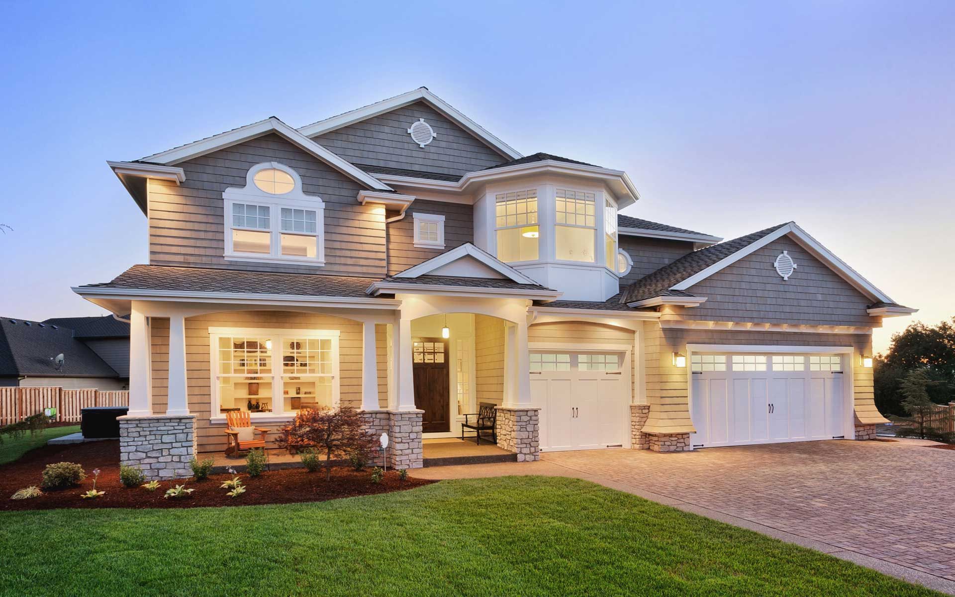 Two-story house with a white garage, gray siding, and a manicured lawn. Dusk lighting.