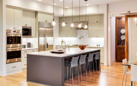 Modern kitchen with island, gray cabinets, stainless steel appliances, pendant lights, and bar stools.