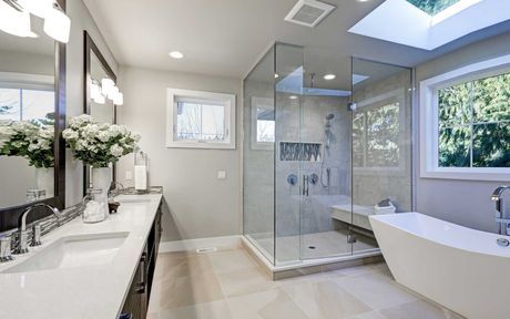 Modern bathroom with white fixtures, glass shower, and skylight.