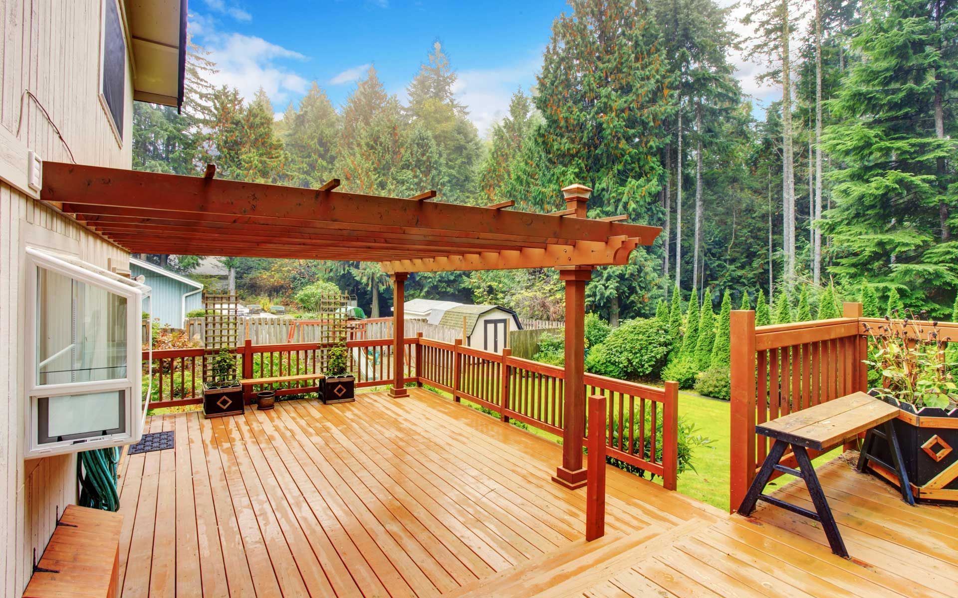 Wooden deck with pergola, railing, and bench overlooking a wooded area.