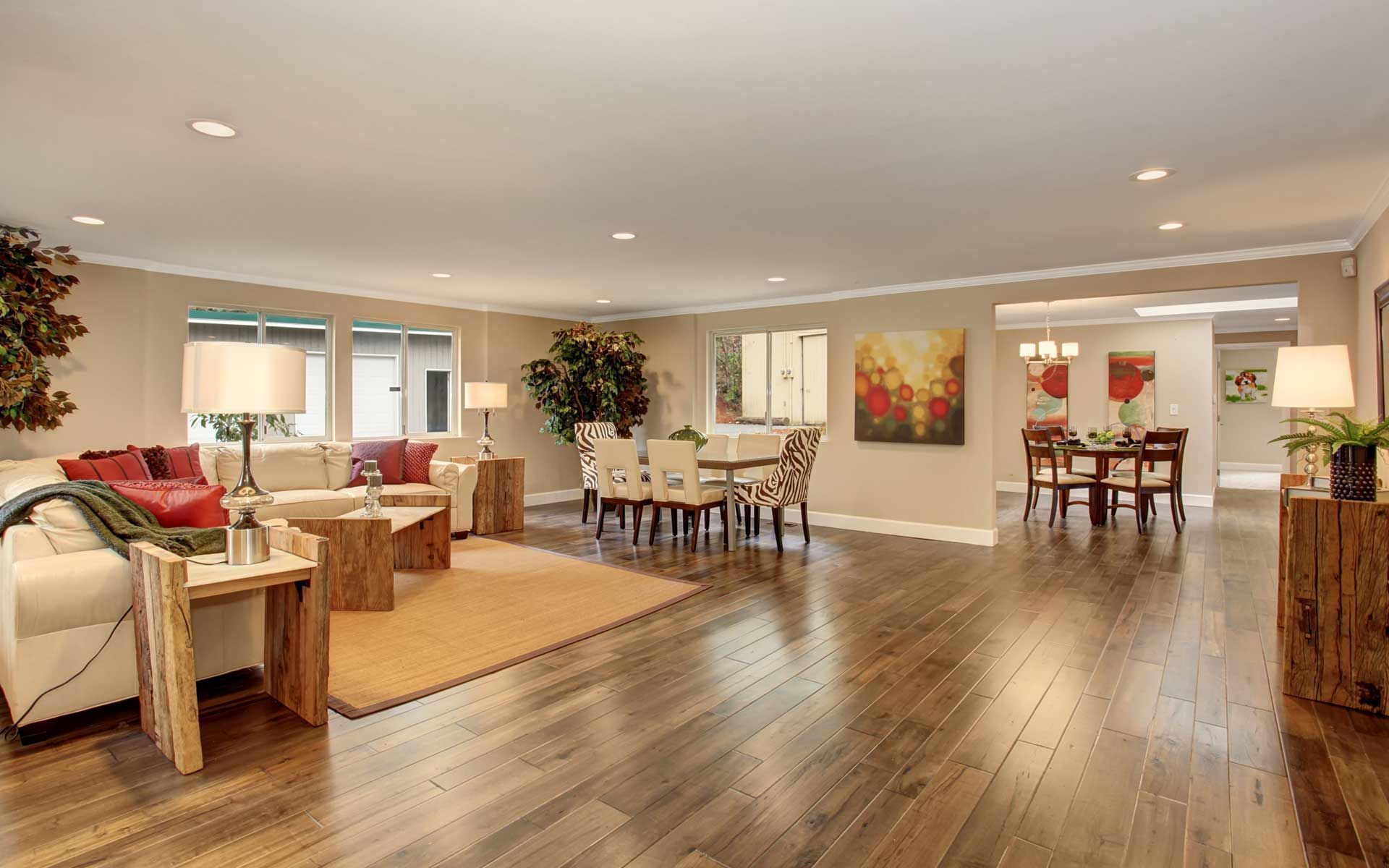 Spacious, open-plan living and dining room with wood floors. Beige walls, light furniture, and a rug.