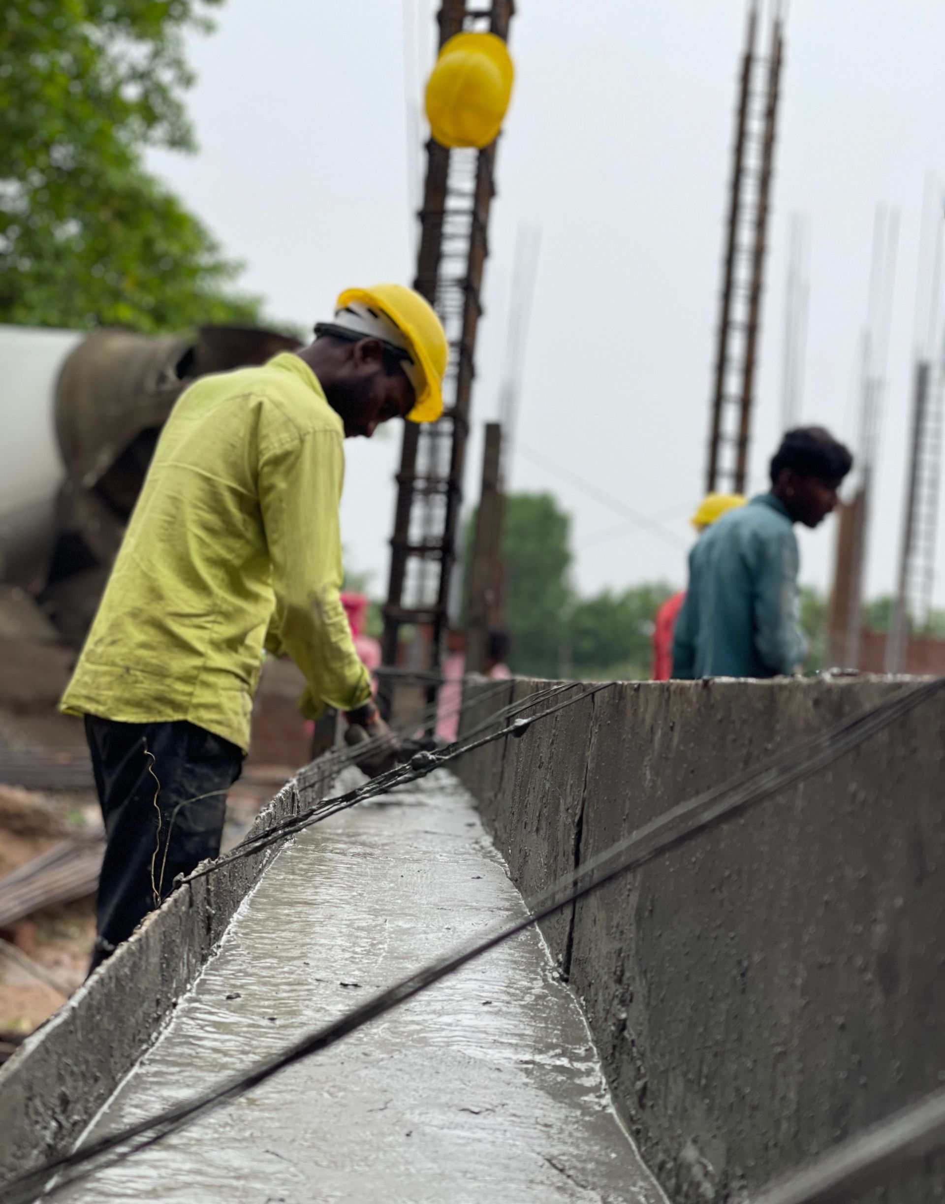 Construction workers pouring concrete into a rebar-lined form at a site under overcast skies