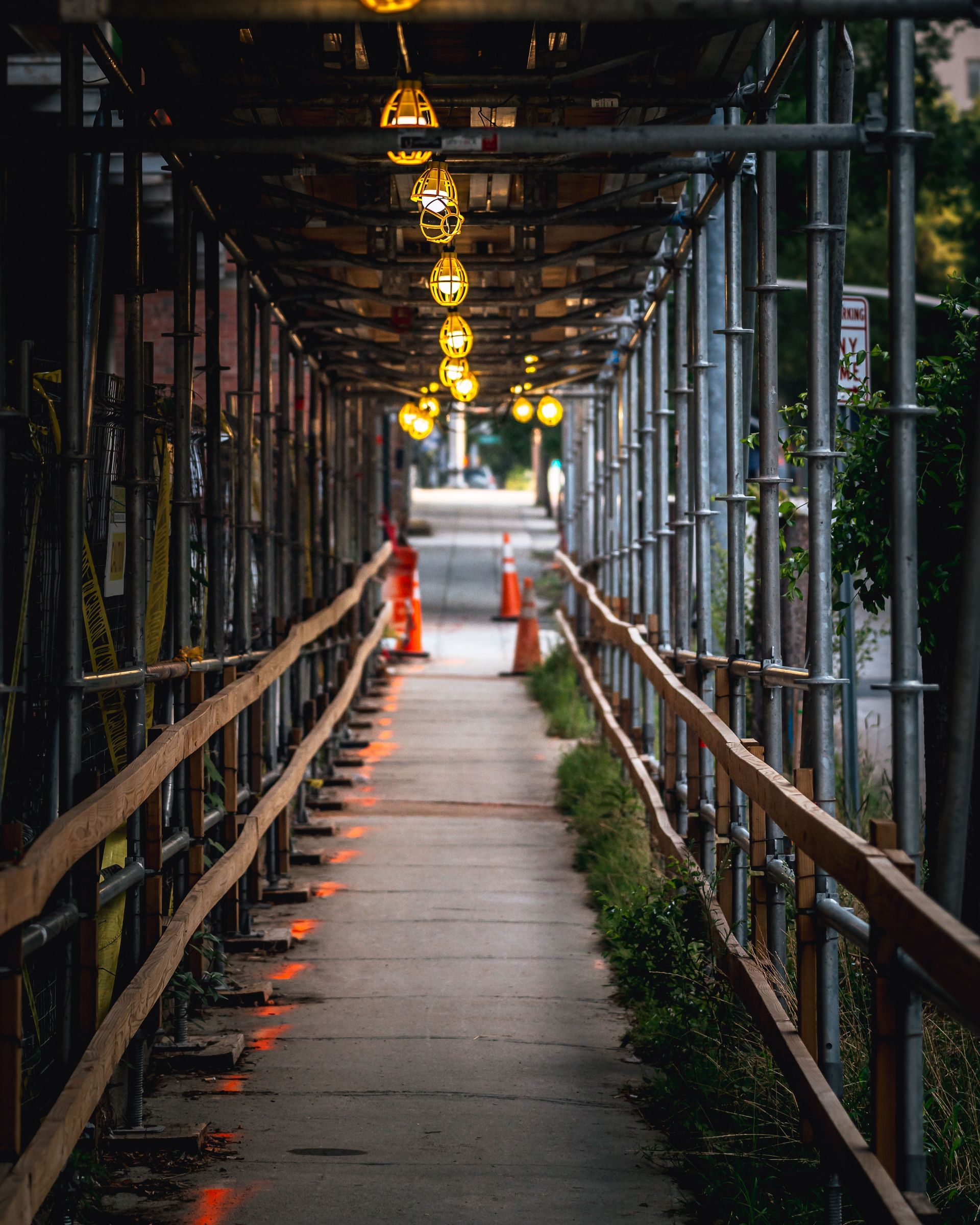 Covered sidewalk with scaffolding and warm hanging lights leading into the distance