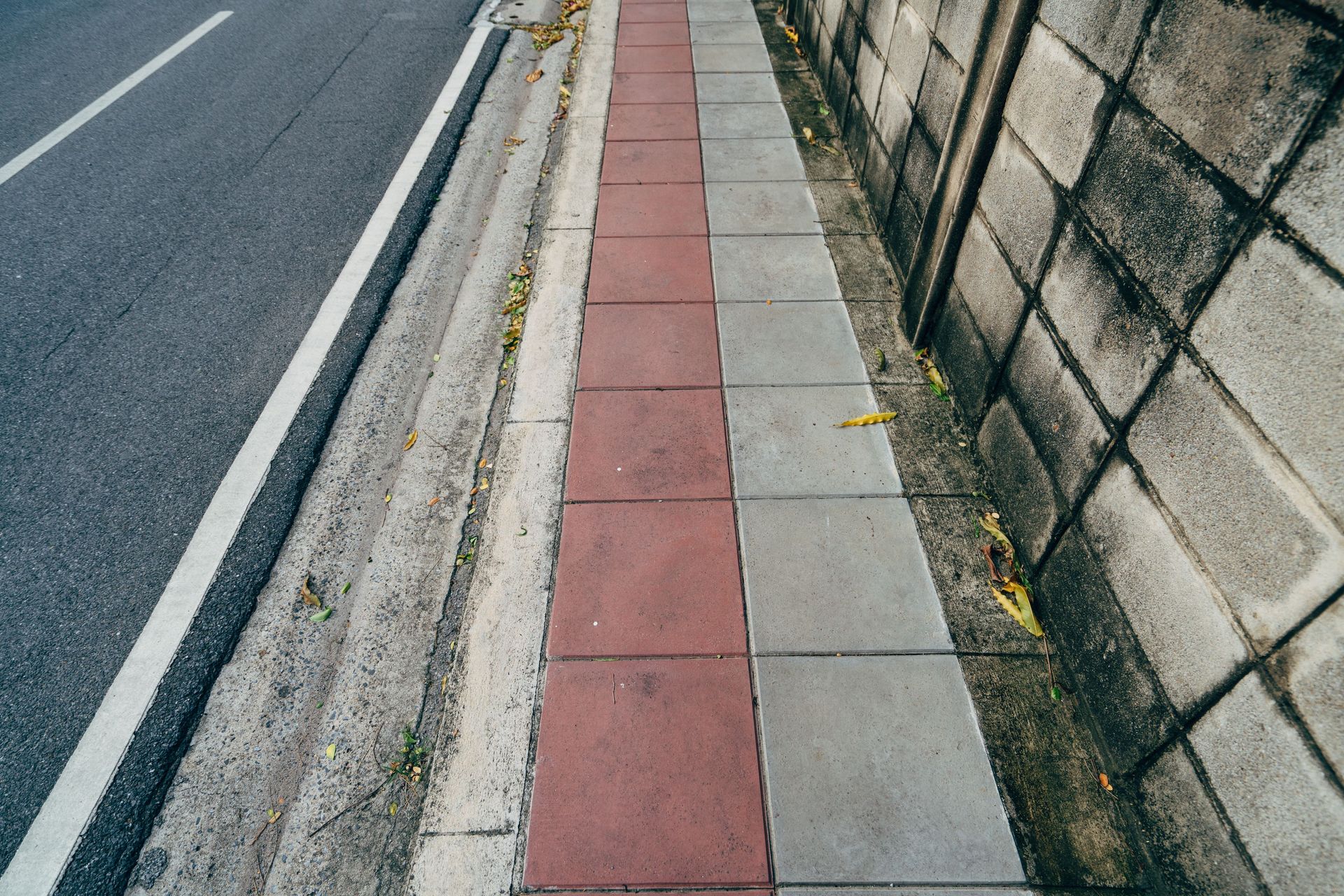 Sidewalk with red and gray paving beside a road and stone wall