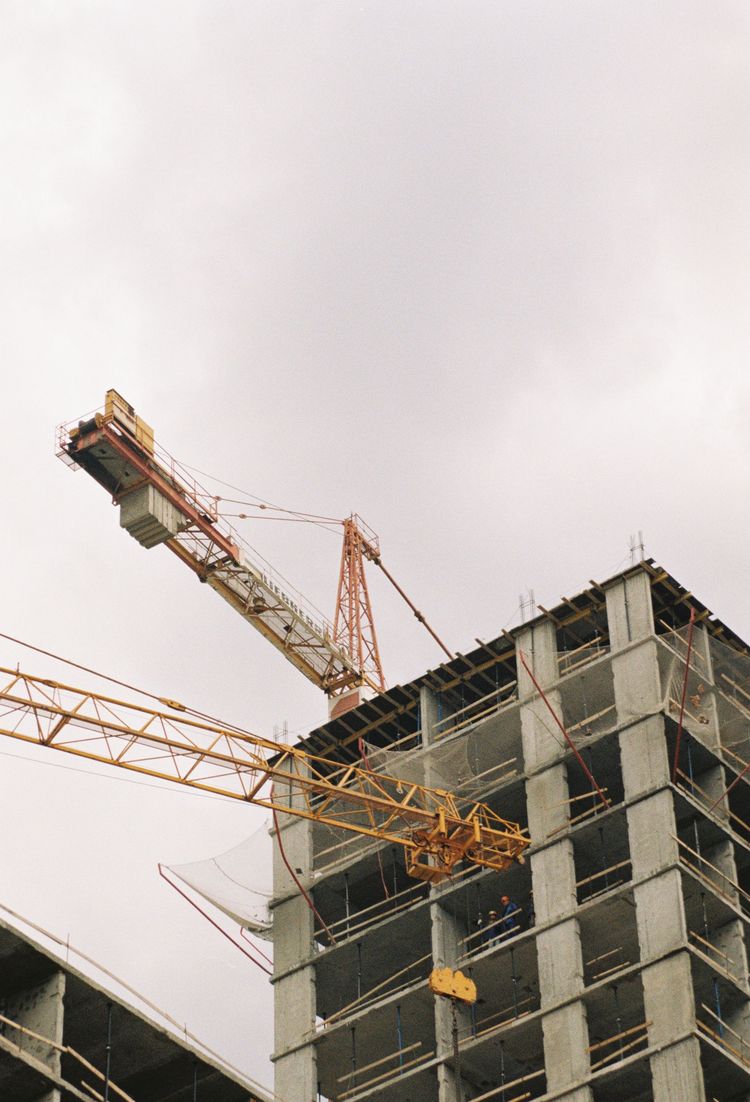 Construction crane beside a high-rise under construction against a cloudy sky