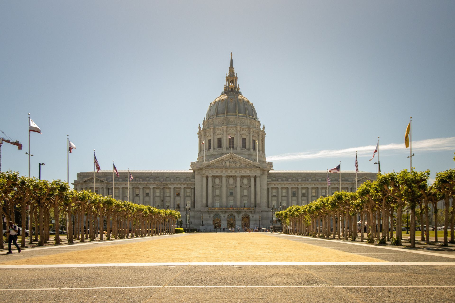 Grand neoclassical civic building with a central dome, seen from a tree-lined plaza on a sunny day