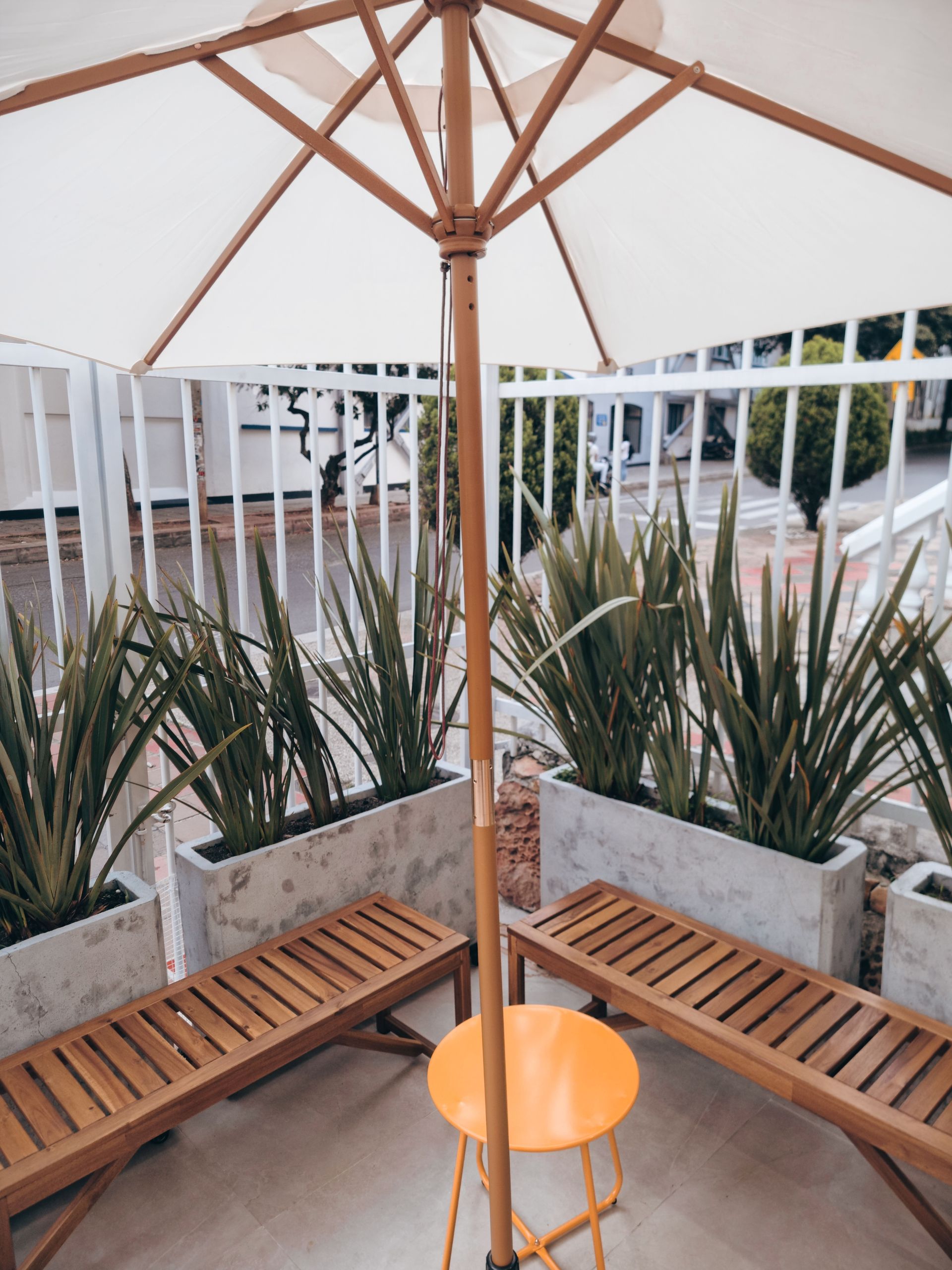 Courtyard seating under a white patio umbrella, with wooden benches and potted plants around the edge