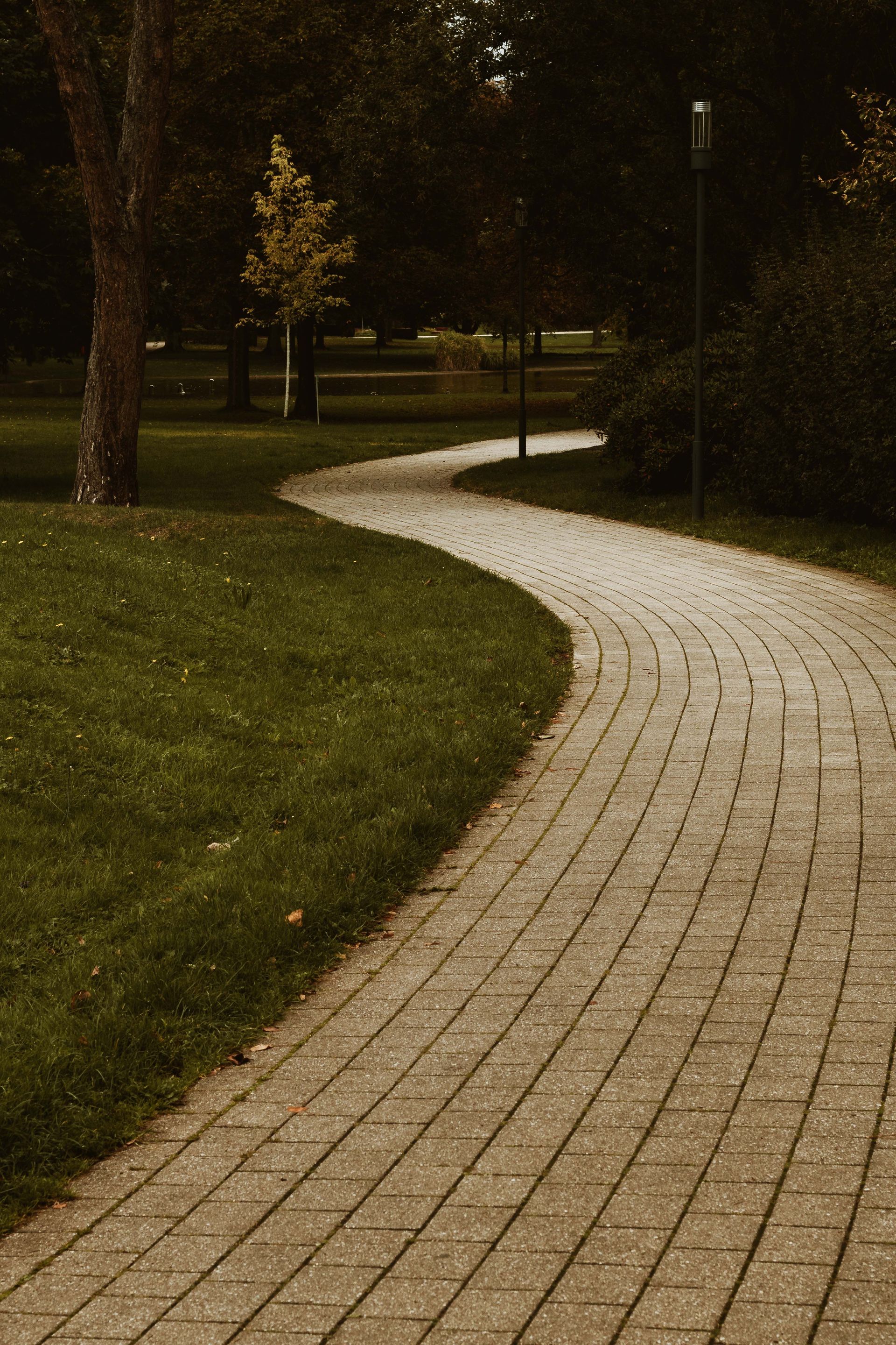 Curving white brick path through a dimly lit park at night