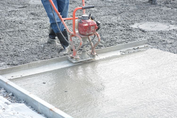Worker using a red concrete screed to smooth wet concrete on a construction site