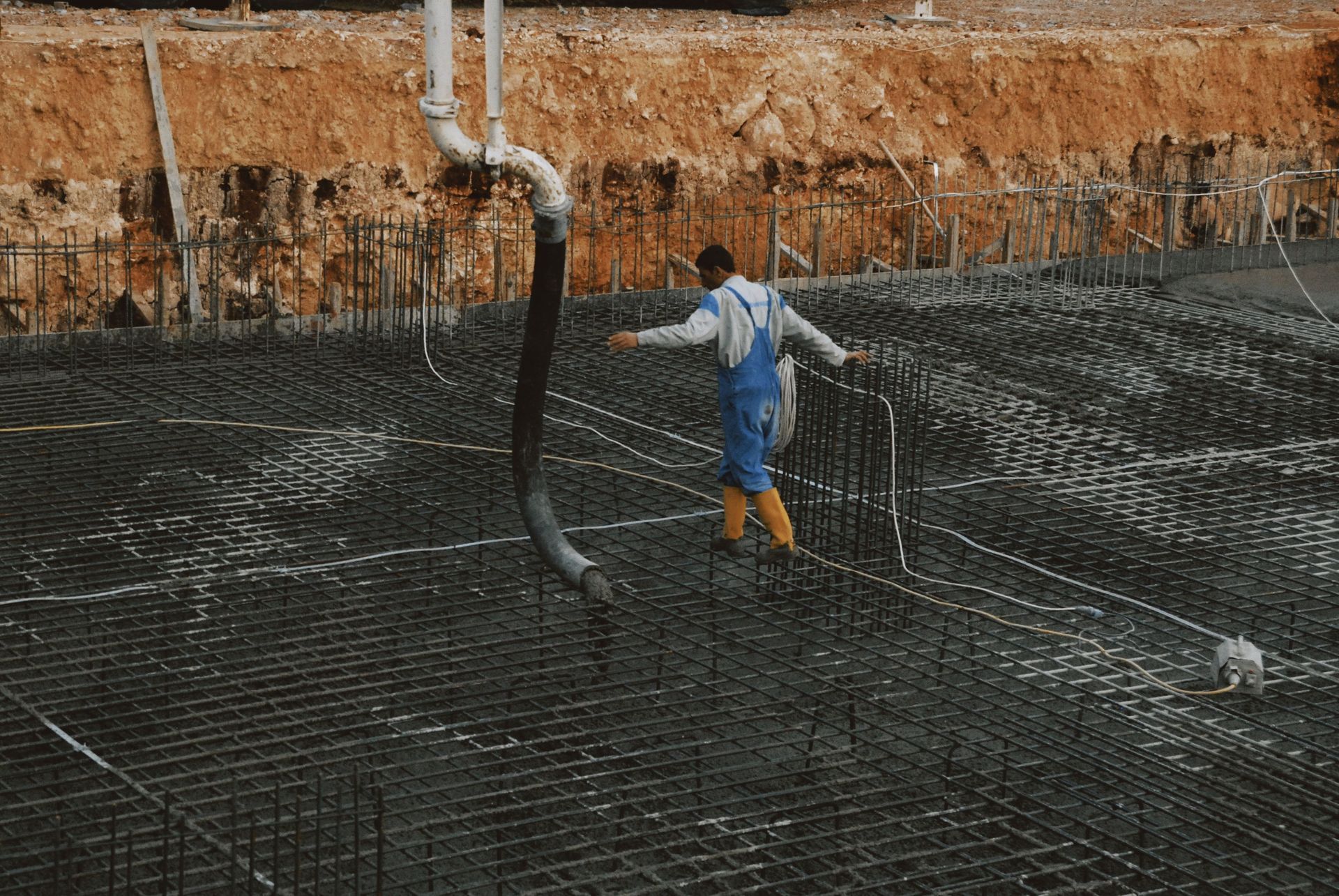 Worker in blue overalls and yellow boots stands in a muddy fish pond with nets and pipes.