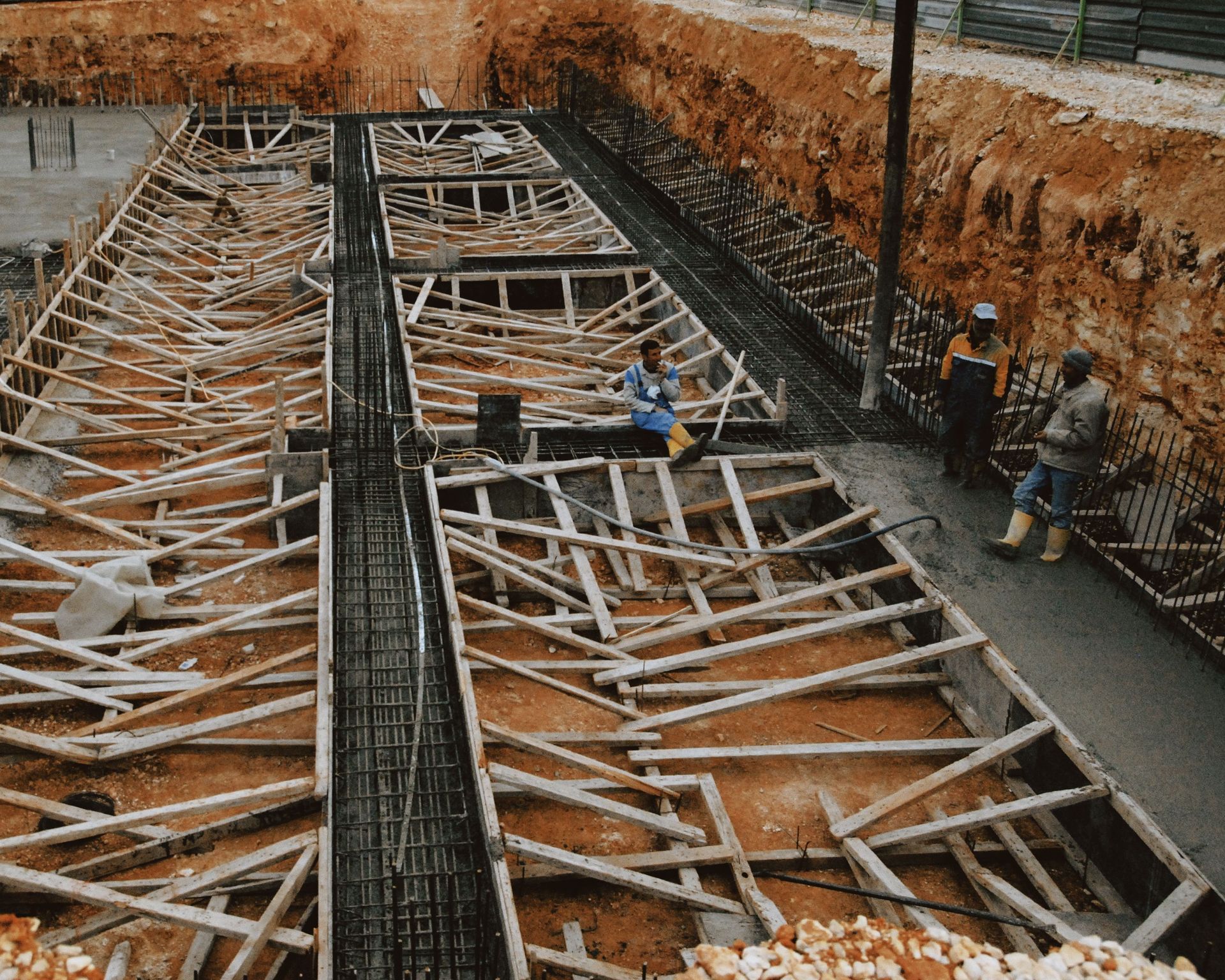 Construction site with workers laying rebar and concrete in deep trenches for a foundation slab.