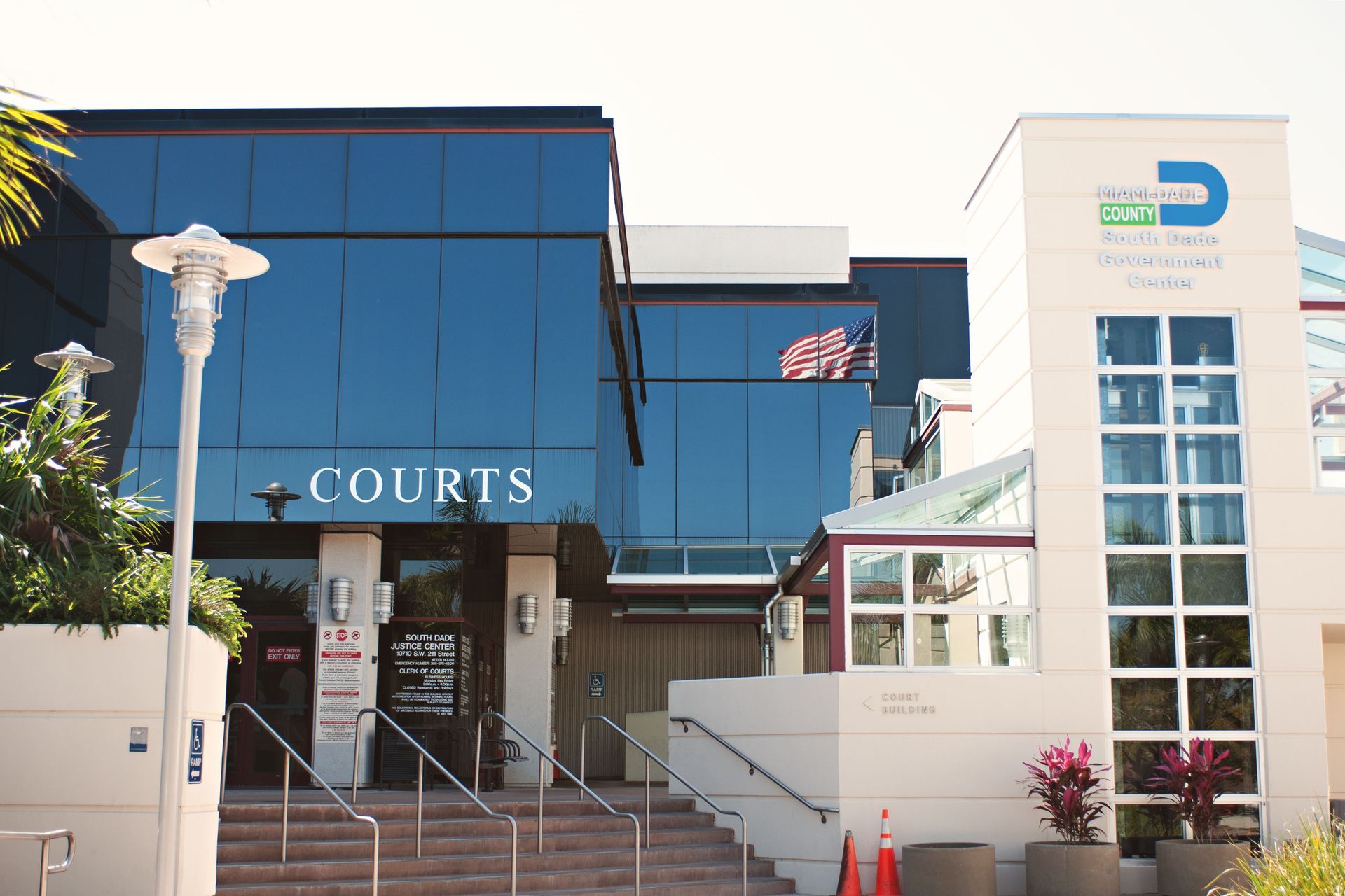 Courts building entrance with blue glass facade and steps, beside a white office tower with logo