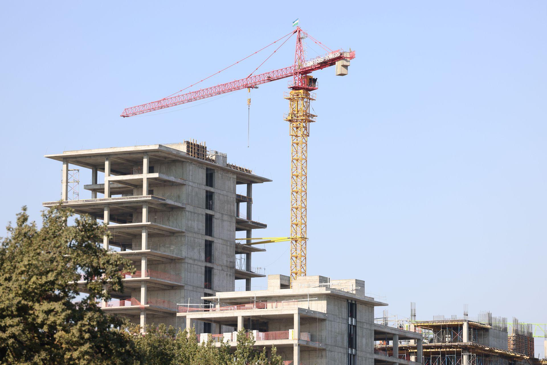 Construction site with a tall crane beside unfinished concrete buildings under a clear blue sky