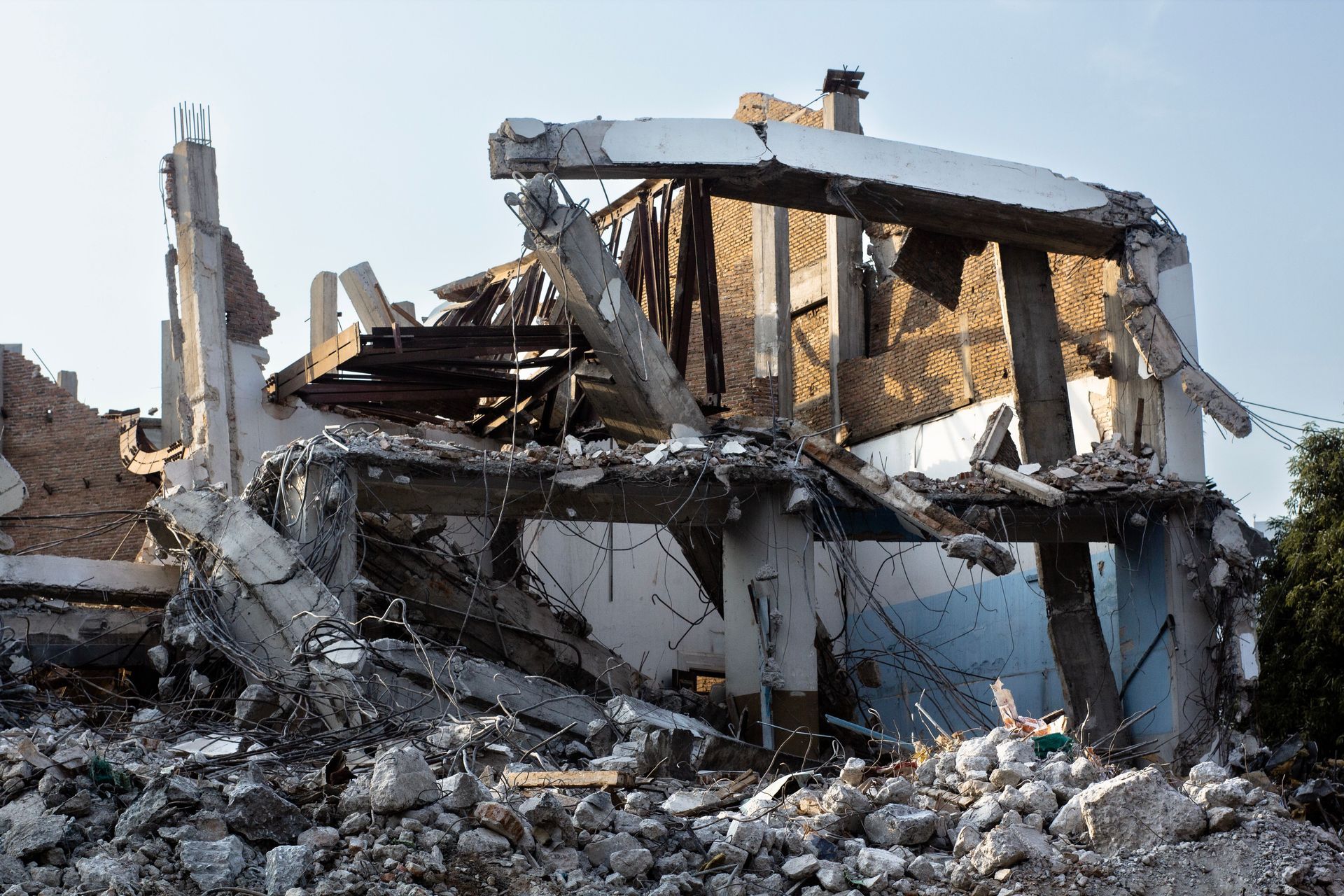 Collapsed concrete building rubble and debris after demolition, with broken walls and twisted beams.