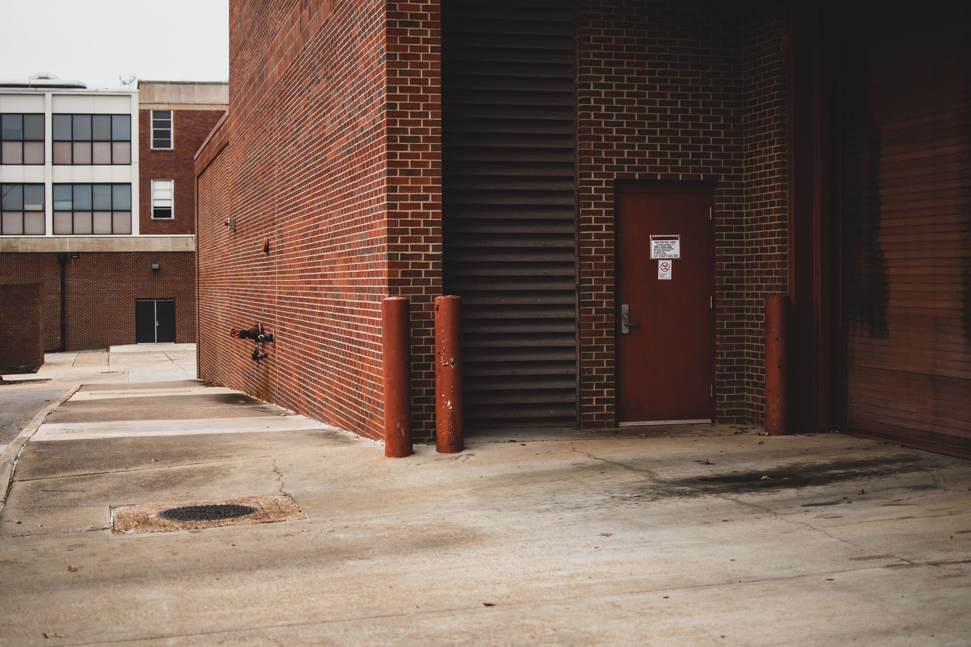Brick building entrance with red door and stairwell, viewed from a concrete courtyard