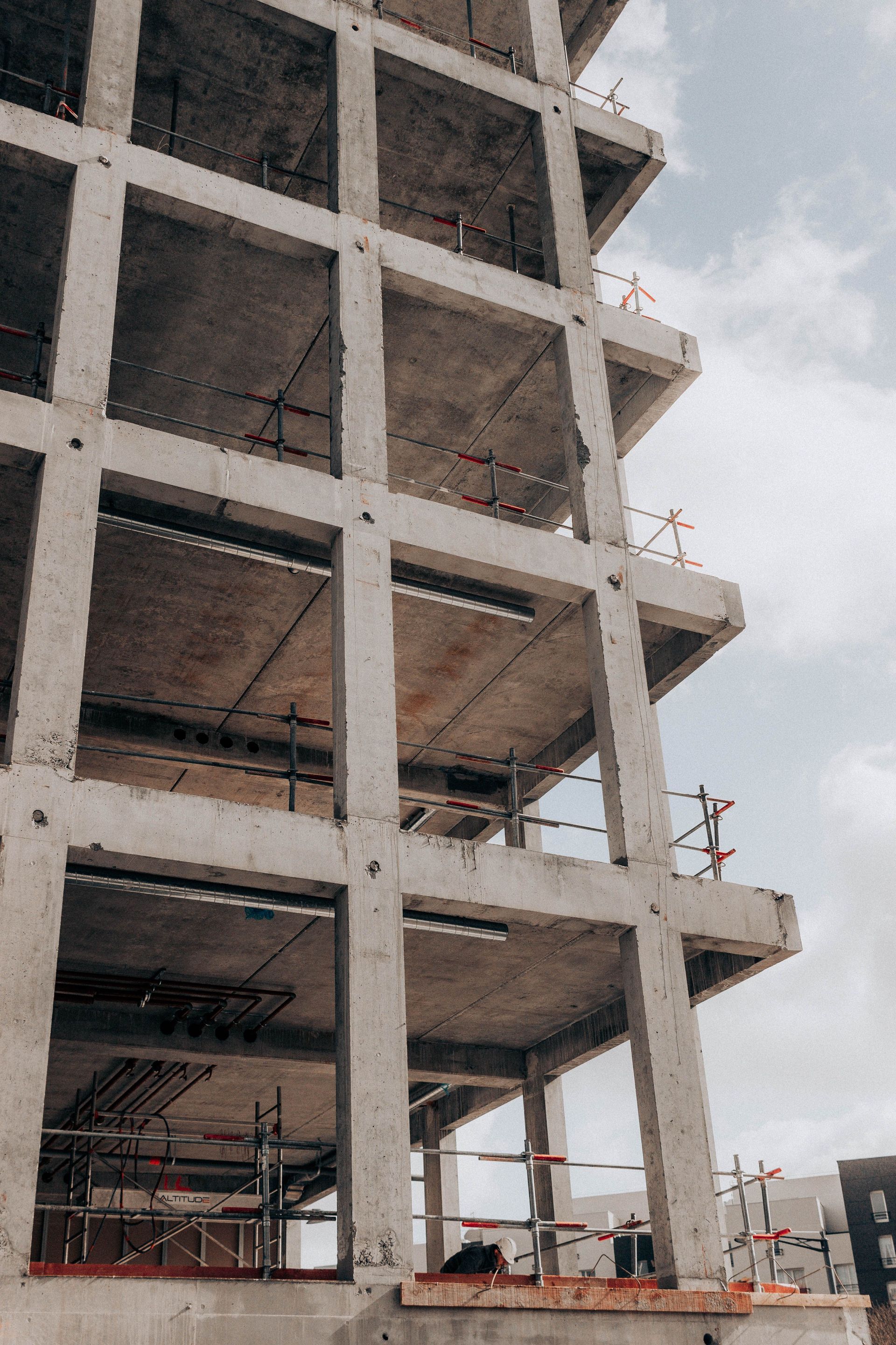 Tall concrete building under construction with exposed floors and workers on scaffolding