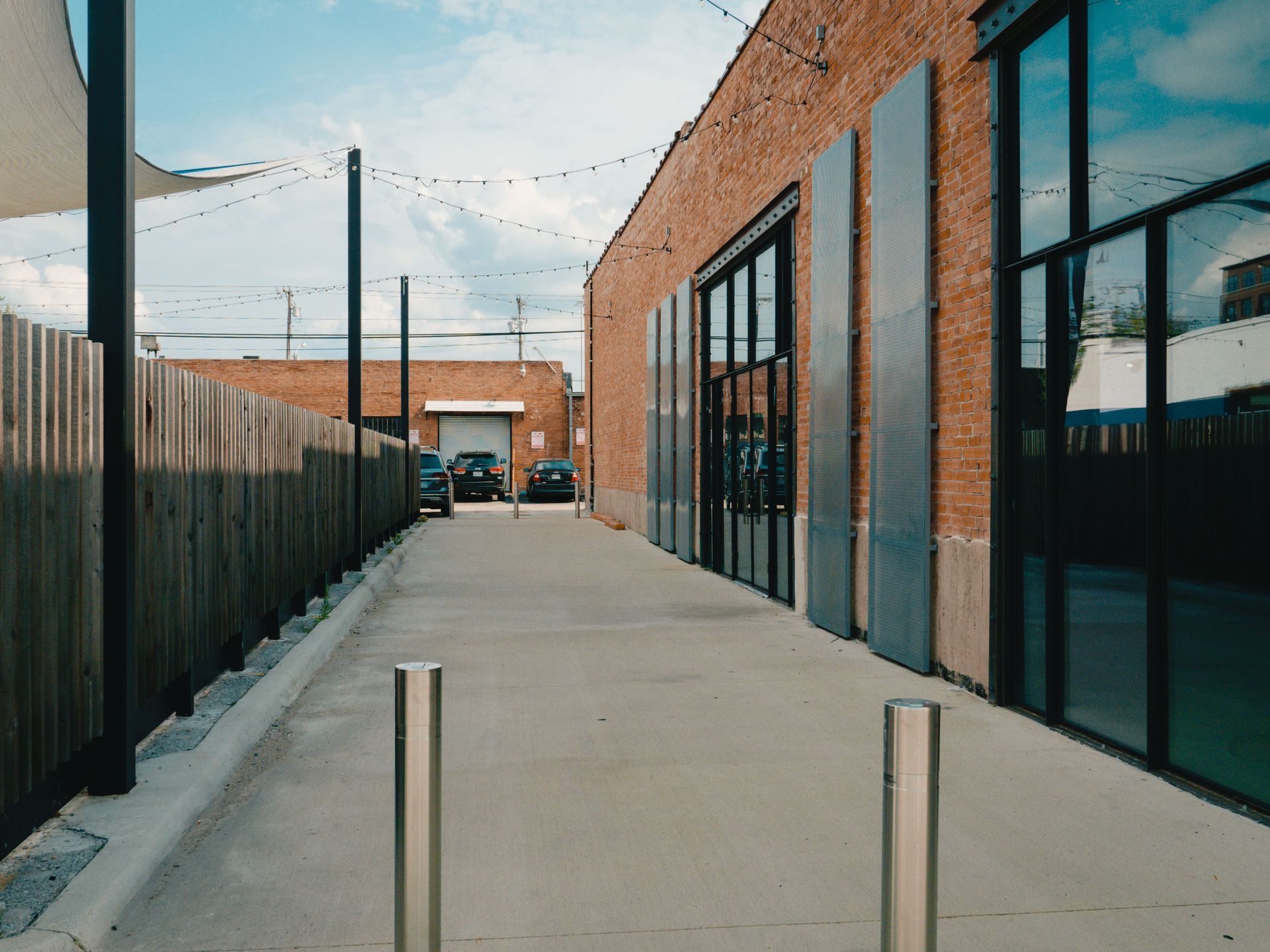 Narrow brick walkway beside glass-front building and fenced alley under string lights