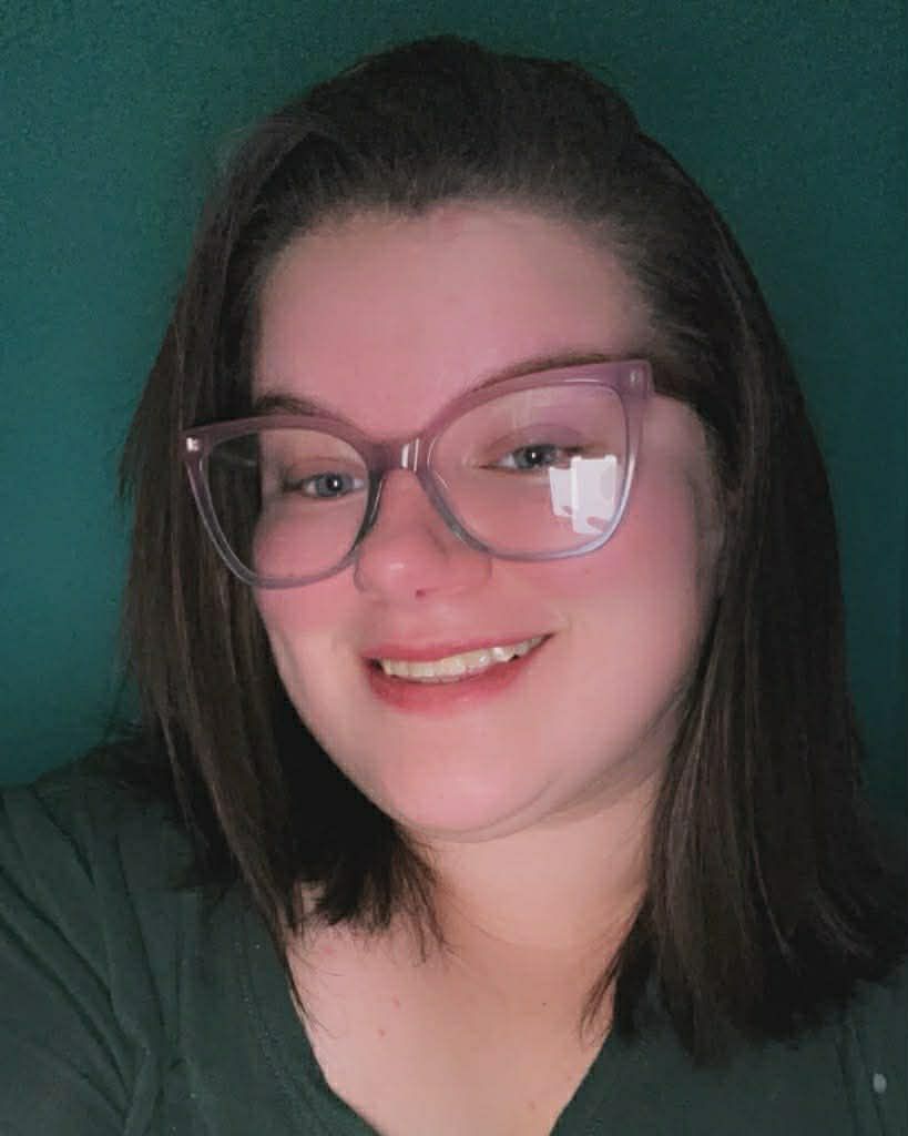 Person wearing glasses smiling in a dark green shirt against a teal background
