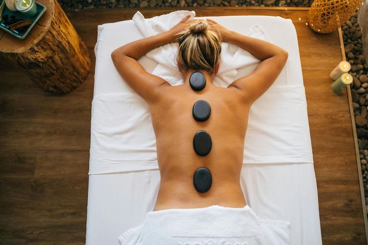 Person lying face down on a massage table with hot stones along their back in a spa setting