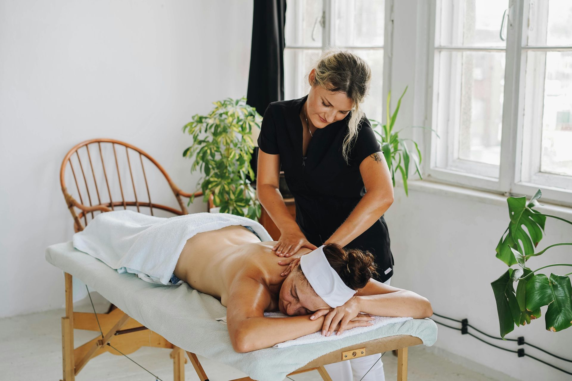 Massage therapist giving a back massage to a client in a bright room with large windows