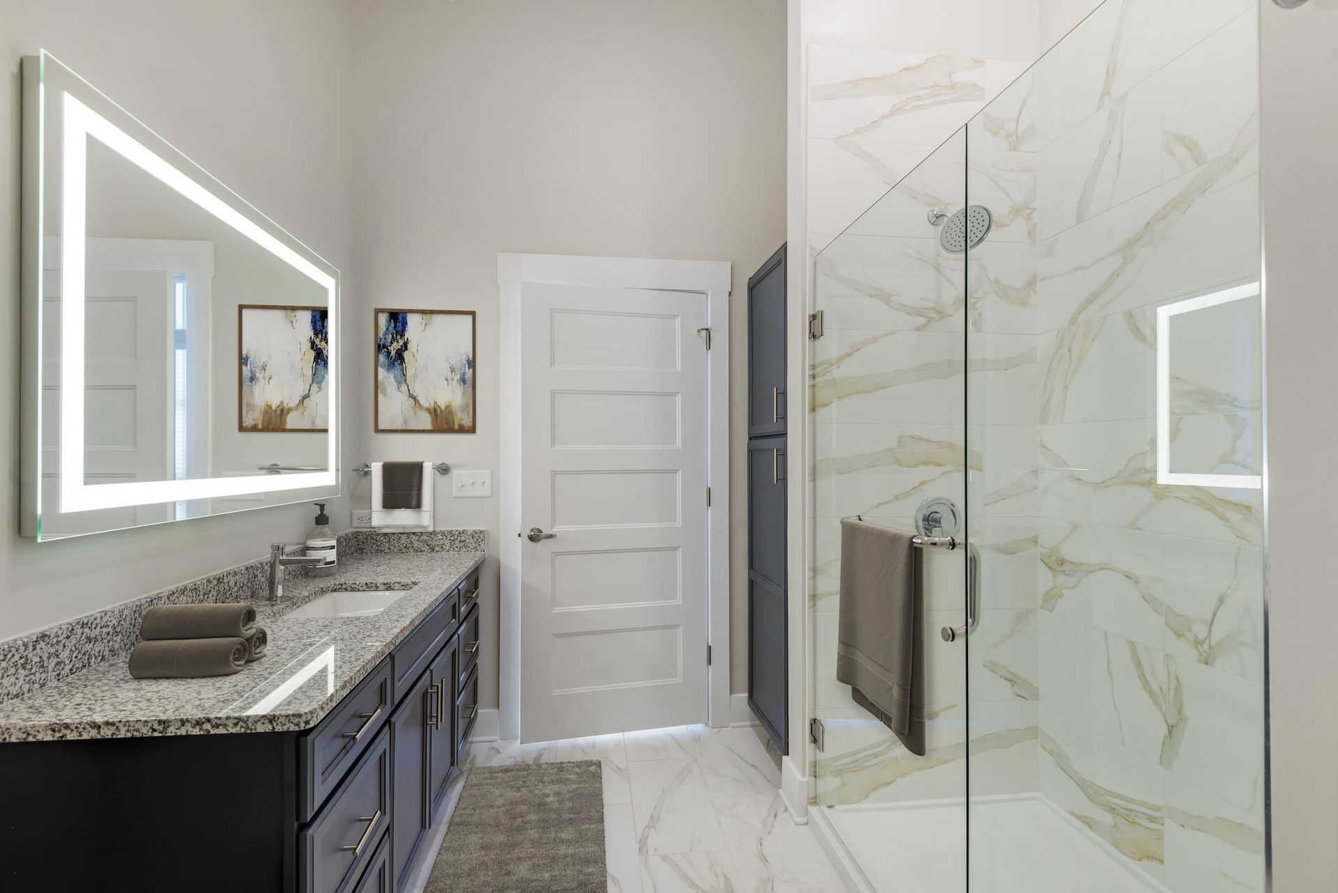 Modern apartment bathroom with a double vanity, backlit mirror, and glass-enclosed marble shower.