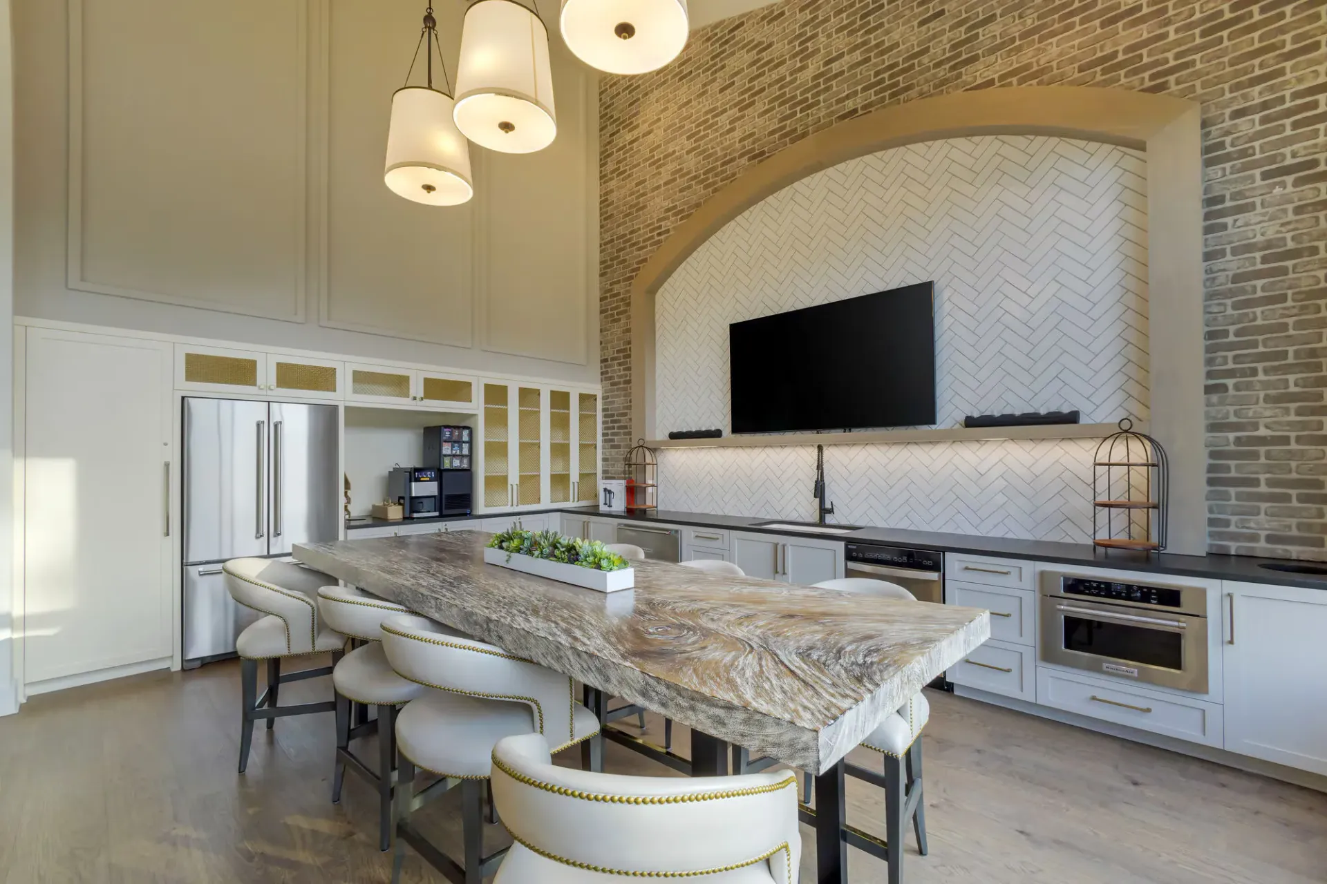 Modern kitchen with a large rustic island, white cabinets, stainless appliances, and a brick arch.