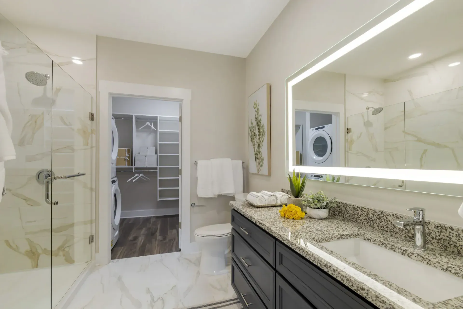 Modern bathroom with marble shower, granite vanity, and a visible laundry closet with a washer/dryer.