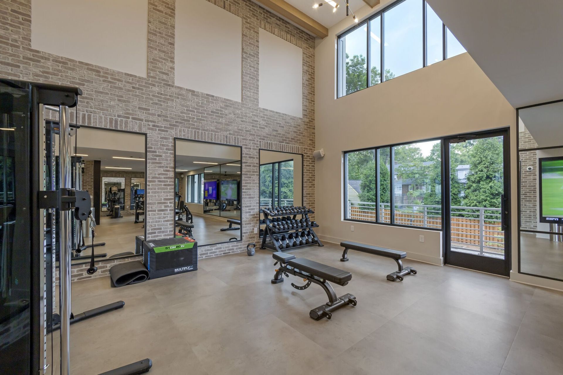 Gym with weight benches, dumbbells, exercise machines, and mirrors. Natural light floods the room.