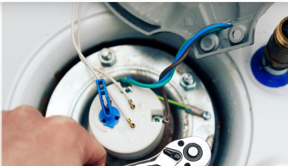 Person using a wrench to work on electrical wiring inside a water heater.