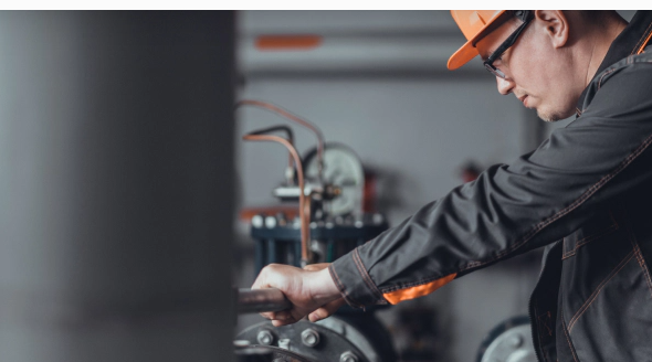 Mechanic in orange hard hat works on machinery.