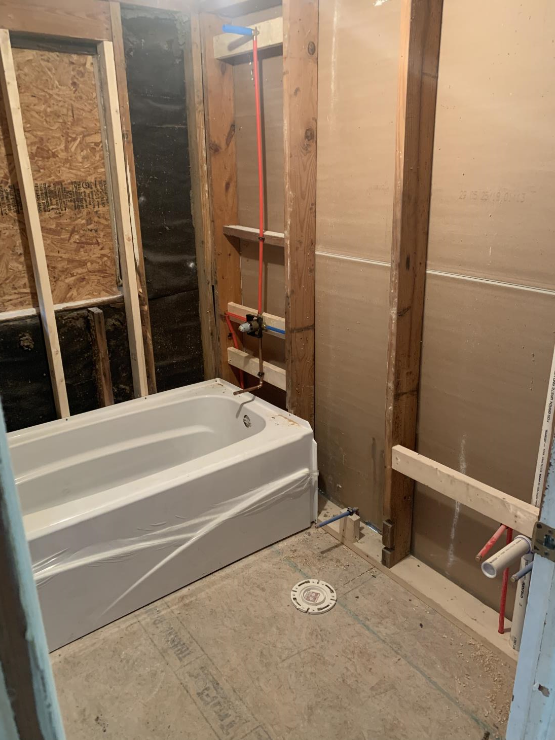 Bathroom renovation: white bathtub in a framed-out space, plumbing visible, unfinished walls.