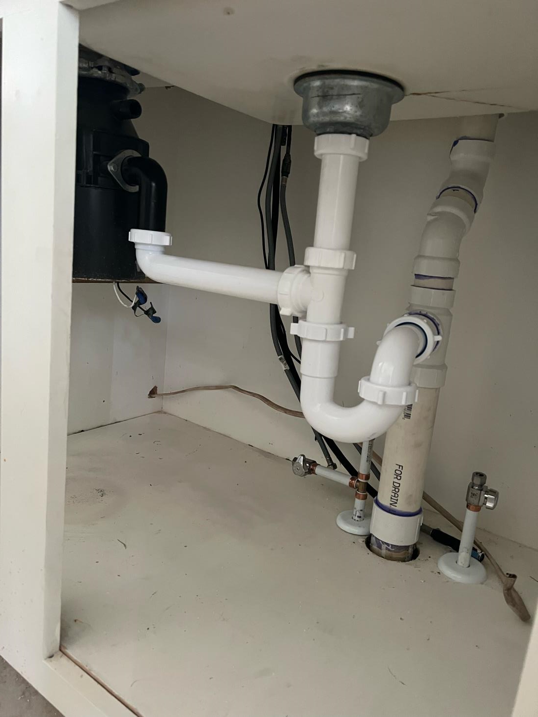 Under-sink plumbing with a garbage disposal, white pipes, and water shut-off valves.