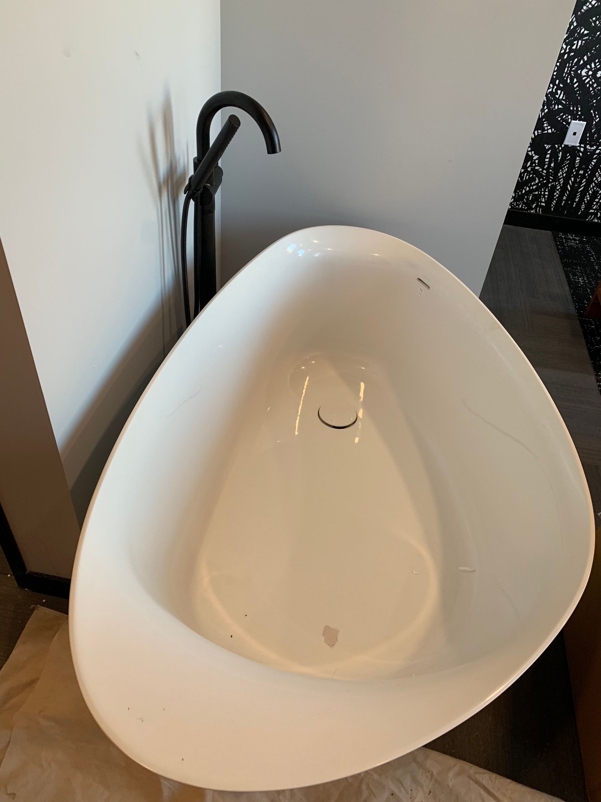 White oval-shaped bathroom sink with black faucet, positioned against a light wall.